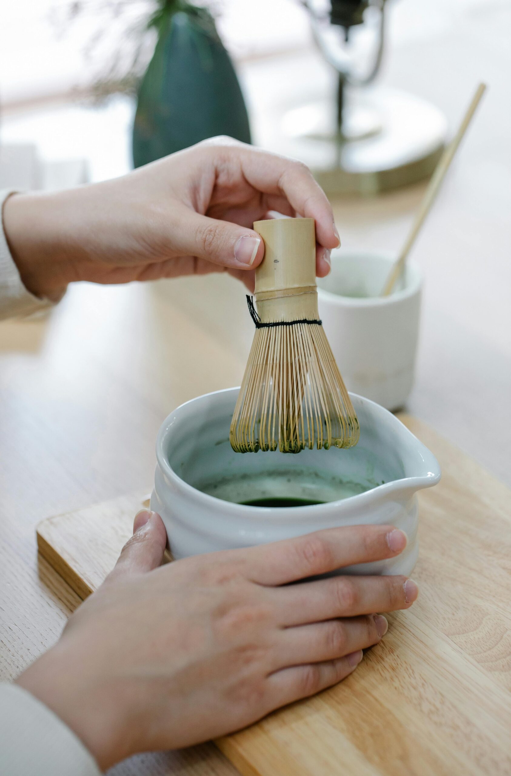 A close-up of a person mixing matcha tea with a bamboo whisk in a bowl.